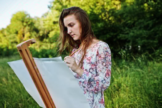 Portrait of an attractive young woman in long dress painting with watercolor in nature. photo
