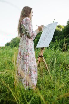 Portrait of an attractive young woman in long dress painting with watercolor in nature. photo
