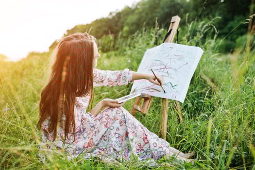 Portrait of a gorgeous happy young woman in beautiful dress sitting on the grass and painting on paper with watercolors. photo