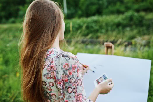 Portrait of an attractive young woman in long dress painting with watercolor in nature. photo