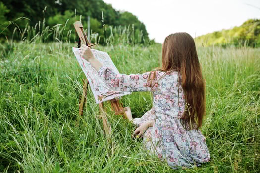 Portrait of a gorgeous happy young woman in beautiful dress sitting on the grass and painting on paper with watercolors. photo