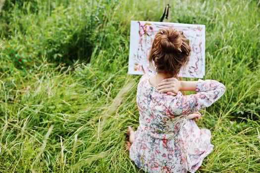 Portrait of a gorgeous happy young woman in beautiful dress sitting on the grass and painting on paper with watercolors. photo