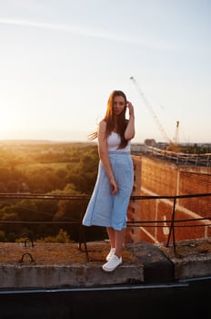Portrait of an outstanding woman in white t-shirt and blue skirt posing on roof at sunset. photo