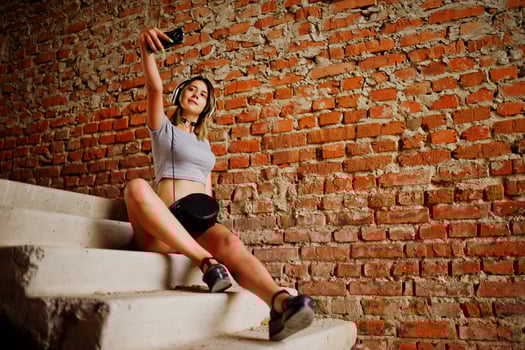 Girl wear on shorts with big headphones make selfie at abadoned factoty with brick walls. photo