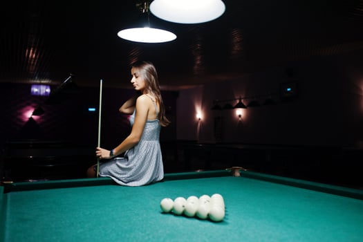 Portrait of an attractive young woman in dress sitting on the pool table and holding a cue. photo