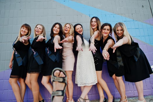 Group of 8 girls wear on black and 2 brides at hen party against colourful wall. photo