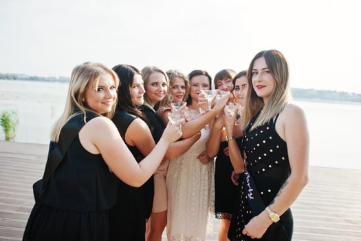 Group of 8 girls wear on black and 2 brides at hen party against sunny beach drinking champagne. photo