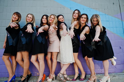 Group of 8 girls wear on black and 2 brides at hen party against colourful wall. photo