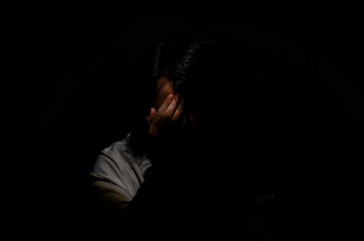Asian miserable depressed man sitting alone in dark background. Depression and mental health concept. photo
