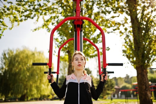 Young girl has the training and doing exercise outdoors on street simulators. Sport, fitness, street workout concept. photo