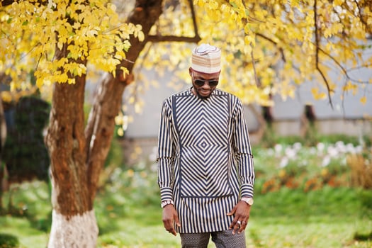 Portrait of stylish black african american man at hat and sunglasses against sunny autumn fall background. Rich people in africa at traditional dress. photo