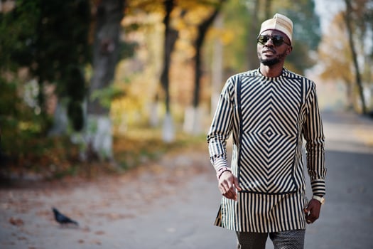 Portrait of stylish black african american man at hat and sunglasses against sunny autumn fall background. Rich people in africa at traditional dress. photo