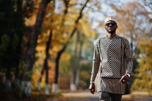 Portrait of stylish black african american man at hat and sunglasses against sunny autumn fall background. Rich people in africa at traditional dress. photo