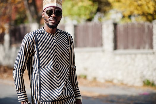 Portrait of stylish black african american man at hat and sunglasses against sunny autumn fall background. Rich people in africa at traditional dress. photo