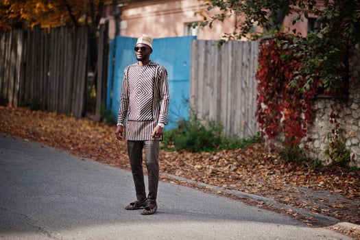 Portrait of stylish black african american man at hat and sunglasses against sunny autumn fall background. Rich people in africa at traditional dress. photo