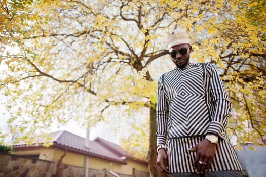 Portrait of stylish black african american man at hat and sunglasses against sunny autumn fall background. Rich people in africa at traditional dress. photo