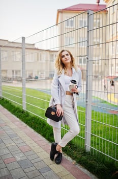 Stylish curly blonde model girl wear on white posing against fence. photo