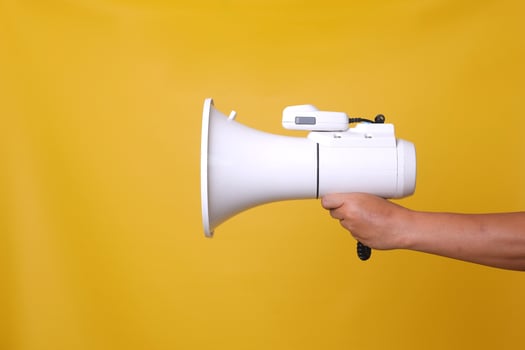 Hand of Asian man holding megaphone over isolated yellow background. photo