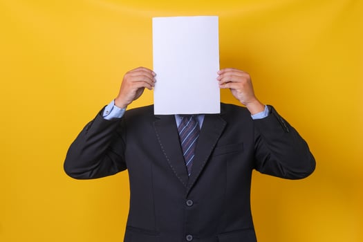 Young businessman in suit  hiding his face under blank sheet paper, isolated yellow background. Mock up and copy space. photo