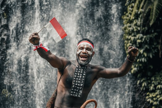 Papua man of Dani tribe is smiling and celebrating Indonesia independence day against waterfall background. photo