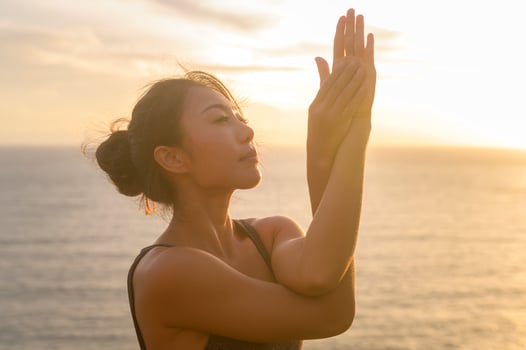Young asian woman in sportswear doing yoga on the rock at seaside during Sunset, health and meditation concept photo