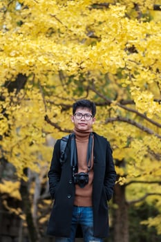 Happy man enjoy at the park outdoor in Autumn season, Asian traveler in coat and camera against Yellow Ginkgo Leaves background photo