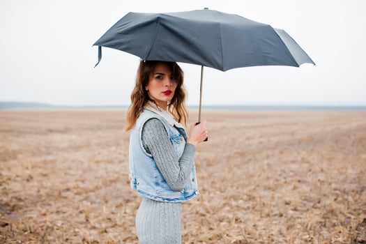 Portrait of brunette curly girl in jeans jacket with black umbrella at field. photo