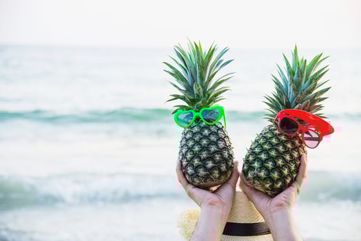 Lovely couple fresh pineapple putting boy and girl glasses in tourist hands with sea wave background - happy fun with healthy vacation concept photo