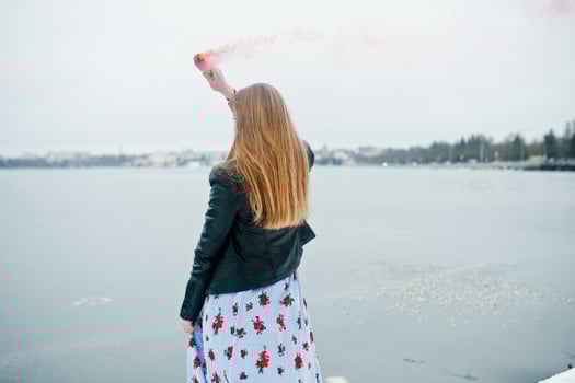 Stylish girl in leather jacket hold pink smoke flare at winter day against frozen lake. photo