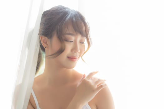 Portrait of beautiful young asian woman makeup of cosmetic, girl hand touch shoulder and smile attractive, face of beauty perfect with wellness in the bedroom with skin care and healthcare concept. photo