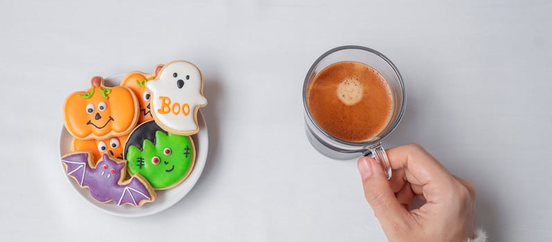 woman hand holding coffee cup during eating funny Halloween Cookies. Happy Halloween day, Trick or Threat, Hello October, fall autumn, Traditional, party and holiday concept photo