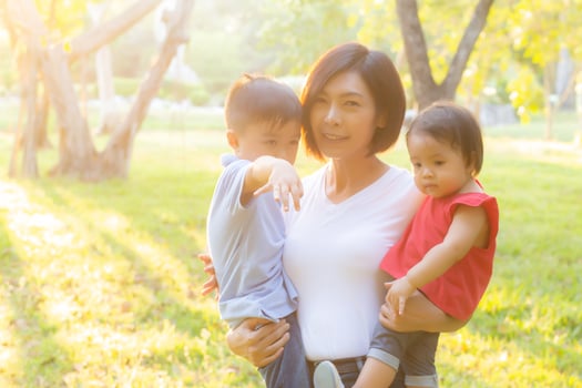 Beautiful young asian mother carrying little boy and girl in the park, asia woman happy having son and daughter and hug kid, mom love and embracing child together, mother day and family concept. photo