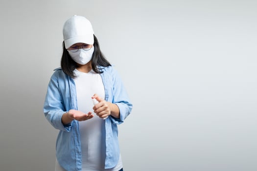 Asian young female in a casual blue t-shirt and white cap is spraying and washing her hand by a small alcohol spray bottle on her hand. white clear background studio light. photo