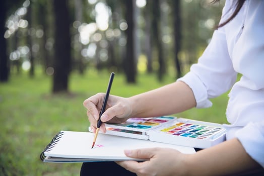 Relax woman painting water colour art work in green garden forest nature - people with creative art in nature stress reduction and meditation concept photo