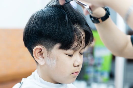 Asian boy is cut his hair in barber shop - people in hairdresser beauty salon concept photo