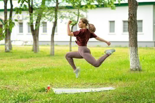 Young girl having online workout outdoors using laptop. Pilates or yoga video lesson on internet. Happy smiling girl practicing pilates lesson online in garden outdoors during quarantine. photo