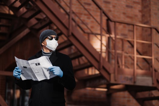 Horiontal shot of pensive man poses with newspaper, wears protective mask and rubber gloves, looks aside, thinks about self isolation, quarantine and coronavirus pandemic. People and covid 19 photo