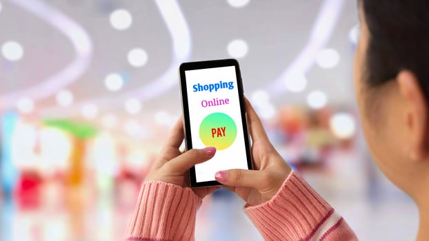 Selective focus at young female hand in pink knitted sweater using application on smartphone to shopping online payment with blurred shopping mall background photo