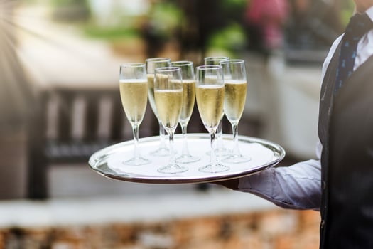 Unrecognizable waiter in formal clothing holds tray with glasses of champagne, carries drinks on festive table to guests, supplies good service for visitors. Hospitality, service and drinking concept photo