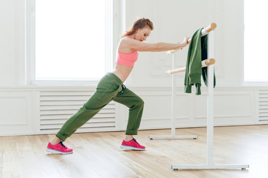 Sport, recreation, flexibility concept. Motivated strong female makes plank, leans at ballet barre, stretches before exercises prepares muscles or biceps for hard training. Aerobics instructor indoor photo