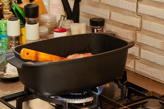 Piece of meat is fried with onions in wine sauce in rectangular pan over fire on gas stove. photo