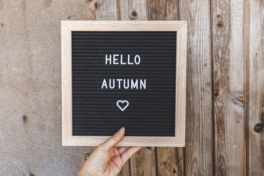Autumnal Background. Woman hand holding black letter board with text phrase Hello Autumn on wooden palnks backdrop. Thanksgiving banner. Hygge mood, cold weather concept photo