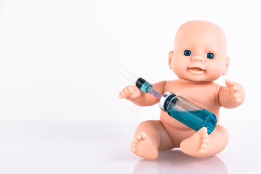 The baby doll is holding a medical syringe and an ampoule with a vaccine. Vaccine for newborns Concept. Copy space. photo