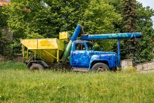 Old heavy truck machinery parked on grass against trees in historic town photo