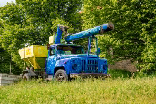 Old blue and yellow truck machinery parked on grass against trees in old town photo
