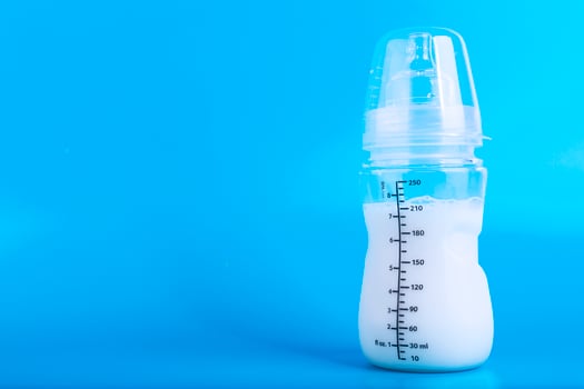 Baby feeding bottle with pacifier on blue background. Copy space. photo