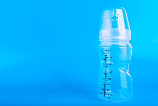 Baby feeding bottle with pacifier on blue background. Copy space. photo