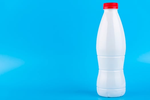 White plastic bottle with red cap for milk on a blue background. Copy space. photo
