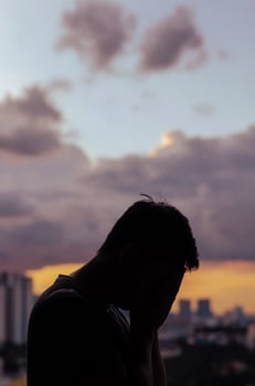 Silhouette of crying depressed man with cloud sky and city background. photo