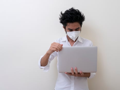 Business man in medical face mask works on laptop at home photo